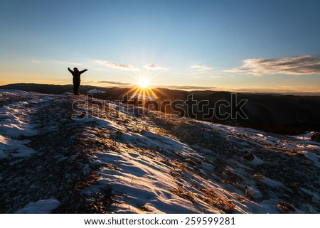 Human silhouette greeting the sunrise in a snowy field in the mountain