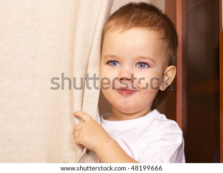 happy little boy looking out from behind curtain
