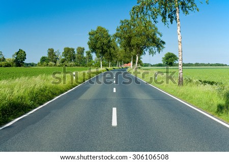 Country-road through northern German lowlands with green fields and trees on a sunny day; Cross-country trip