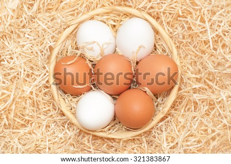 White and brown hen\'s eggs in a round wicker basket with wood wool; Easter eggs in natural colors