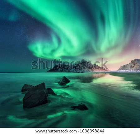 Aurora. Northern lights in Lofoten islands, Norway. Sky with polar lights, stars. Night winter landscape with aurora, sea with sky reflection, stones, sandy beach and mountains. Green aurora borealis