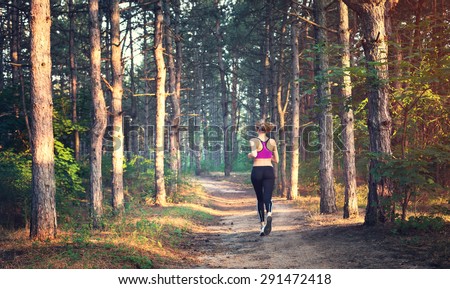Young woman running on a rural road at sunset in summer forest. Lifestyle sports background
