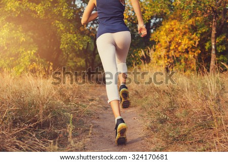 Young woman running on a rural road at sunset in autumn forest. Lifestyle sports background