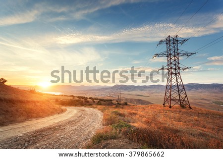 High voltage tower in mountains on the background of colorful sky at sunset.  Electricity pylon system. Summer evening. Industrial landscape