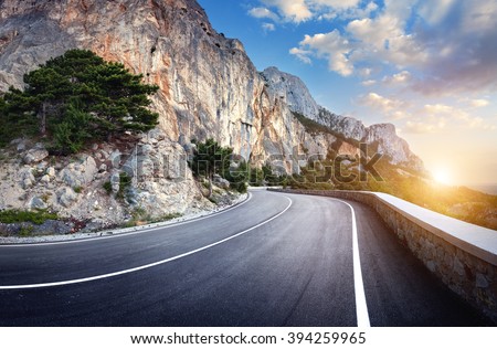 Beautiful winding mountain road with a perfect asphalt with high rocks and colorful sunset in summer.