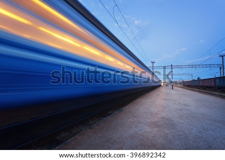 Colorful high speed passenger train on tracks in motion at rural railway station at sunset