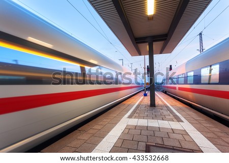 High speed passenger trains on railroad platform in motion at dusk. Blurred commuter train. Railway station in Nuremberg, Germany. Industrial landscape