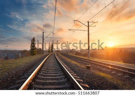 Railroad against beautiful sky at sunset. Industrial landscape with railway station, colorful blue sky with clouds, trees and green grass, yellow sunlight. Railway junction. Heavy industry. Travel