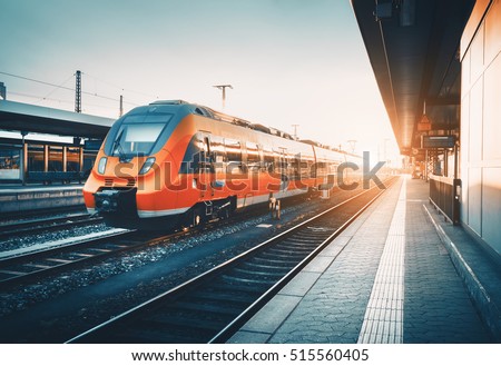 Modern high speed red commuter train at the railway station at colorful sunset. Railroad with vintage toning. Train at railway platform. Industrial landscape. Railway tourism. Vintage toning. Concept