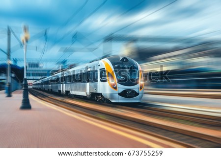 High speed train at the railway station at sunset in Europe. Modern intercity train on railway platform. Urban view with beautiful passenger train on railroad and buildings. Railway transportation