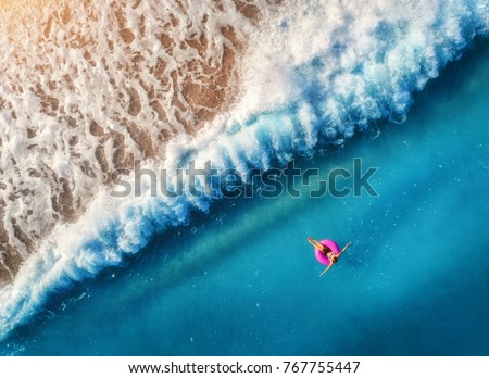 Aerial view of young woman swimming on the pink swim ring in the transparent blue sea in Oludeniz,Turkey. Summer seascape with girl, beautiful waves, azure water at sunset. Top view from drone. Travel