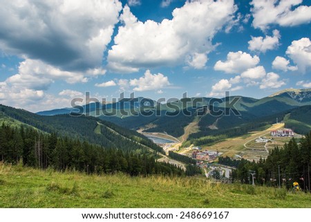 Mountain landscape with cloudy sky, forest and mountain lake overlooking the ski resort in summer
