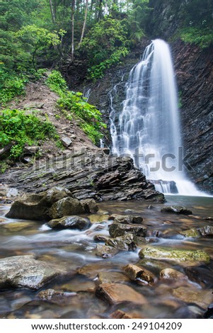 Great mountain waterfall, rolling in mountain river with blurred water and rocks in the foreground