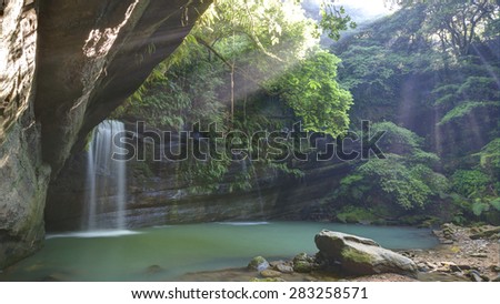 A waterfall in a mysterious forest with sunlight shining through the greenery