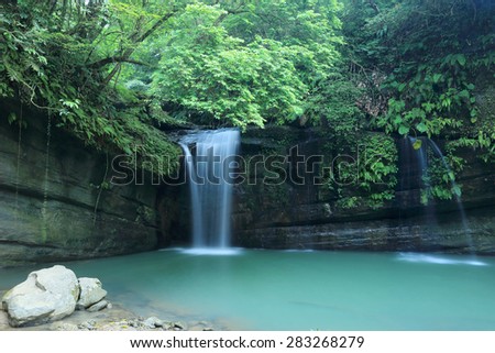 A cool refreshing waterfall and an emerald pond in a mysterious forest of lush greenery