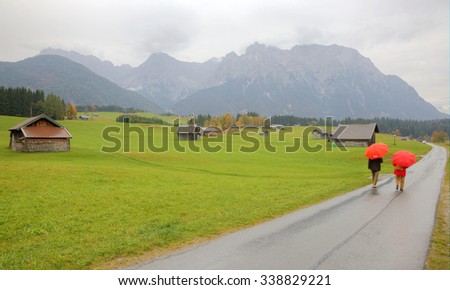 Autumn scenery of a ranch farmland near Mittenwald in a foggy drizzling morning ~ a road passing through a meadow with wooden barns and Karwendel mountains in the background in Bavaria, Germany