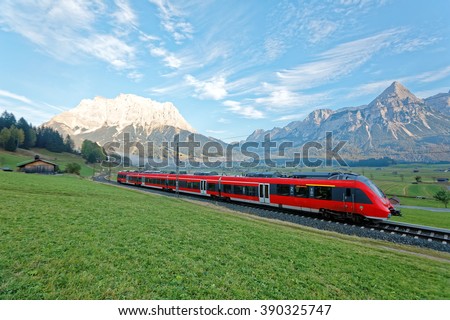 Panoramic view of a train traveling on green fields with Mountain Zugspitze in background on a beautiful sunny day in Lermoos, Tirol Austria ~ Beautiful autumn scenery of idyllic Tyrolean countryside