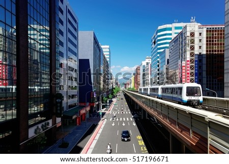 View of a train traveling on elevated tracks of Taipei Metro System between office towers under blue clear sky ~ View of MRT railways in Taipei, the capital city of Taiwan, on a beautiful sunny day