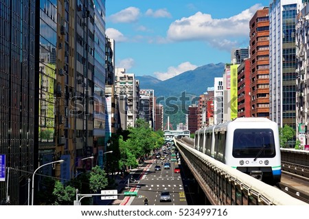 View of a train traveling on elevated rails of Taipei Metro System between office towers under blue clear sky ~ View of MRT railways in Taipei, the capital city of Taiwan, on a beautiful sunny day