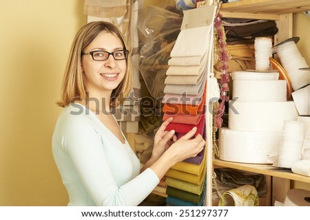 Young seamstress is choosing the cloth for sew and smiling into the camera