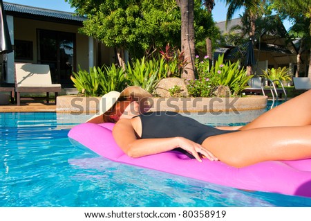 Woman with hat relaxing in outdoor swimming pool on air mattress