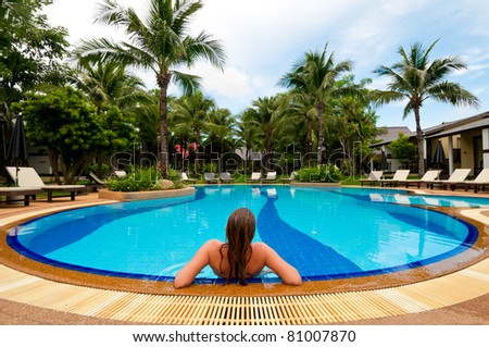 Woman relaxing in blue outdoor swimming pool. Back view