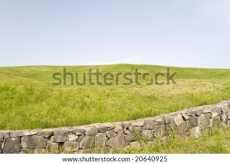 green landscape with a blue sky and a stone wall