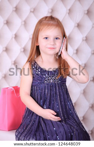 Red haired little cute girl talking on the phone after shopping in a store