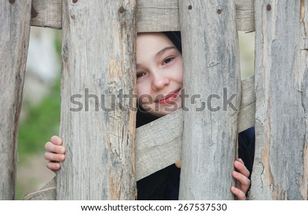 Little Girl Peeking Over an Old Wooden Fence with a Smile While Looking at the Camera.