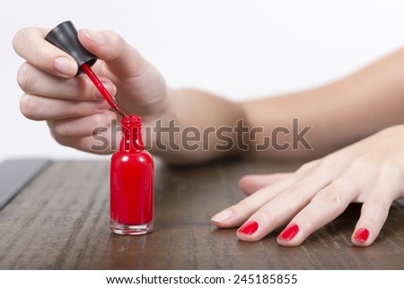 A hand applying red nail polish on a table