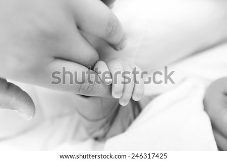 Black and white photo of a baby\'s hand holding the finger of his dad or his mom
