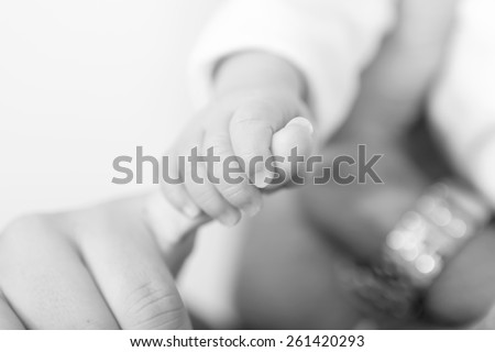 Black and white photo of a baby\'s hand holding the finger of his dad or his mom with shallow depth of field