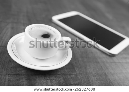 Black and white photo of a no name coffee cup and a tablet in background on a wood table with shallow depth of field