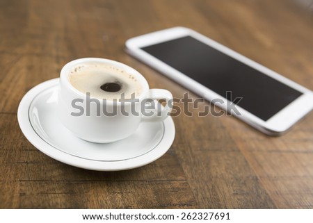 Photo of a no name coffee cup and a tablet in background on a wood table with shallow depth of field