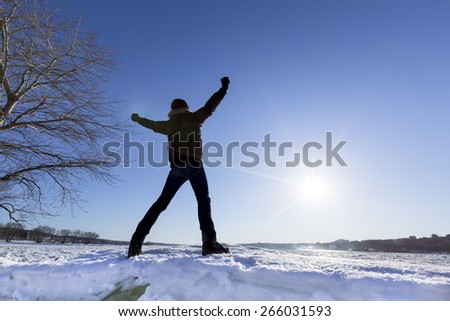 Photo of a free man standing on a pile of snow with his hands raised to heaven and the sun on his face