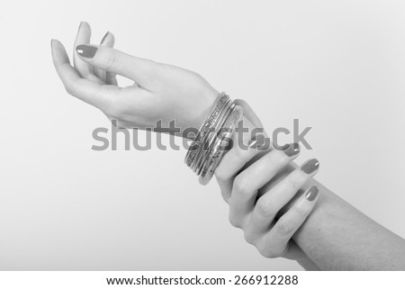 Black and white photo of a woman with nice nails showing jewel on her arm with her hands on a light gray background