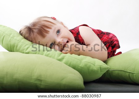 18 month old baby girl in red checked dress on green pillows on white background