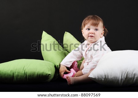 18 month old baby girl dressed in bath robe on green and white pillows on black background
