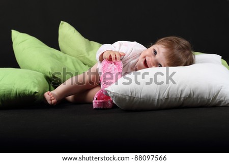 18 month old baby girl dressed in bath robe on green and white pillows on black background