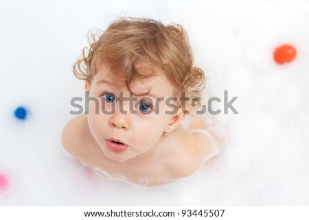 20 months year old baby girl in the bath full of foam with color toys looking upwards