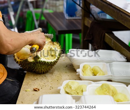 A fruits shop owner is using knife to peel durian in the wet market in Singapore. After peeling durian are packaged into fresh to-go, ready to eat, convenience packs and sell locally