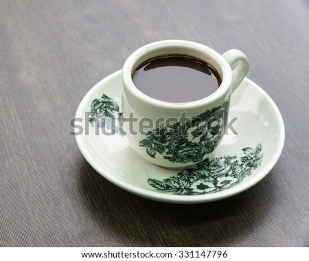 Traditional Singapore kopitiam (or kopi tiam) style milk coffee in vintage mug, fractal on the cup is generic print. Close-up view with dramatic, ambient light on wooden background