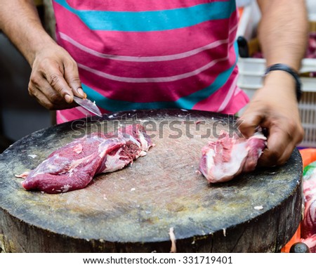 Close-up view hands of pork shop owner is using knife to cut slices of raw meat on a wooden cutting board