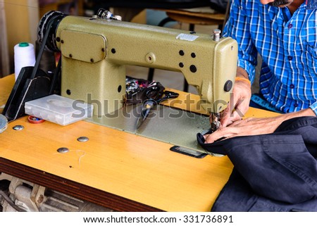 Close-up view of man hand with sewing machine in action. He is repairing a sewing black fabric on an old sewing machine