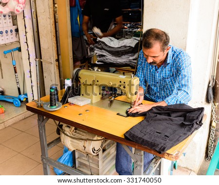 SINGAPORE OCT 26, 2015: An Indian man is repairing a sewing black fabric on an old sewing machine at the roadside of Little India in Singapore