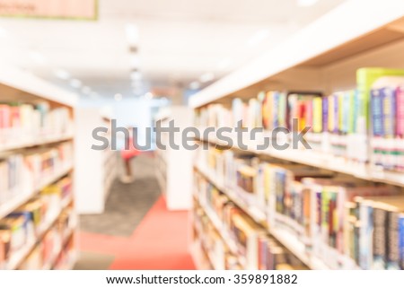 Blurred abstract background of public library interior with aisle of bookshelf with textbooks, literature, magazines. Female student is selecting books from bookshelf. Self-study education concept