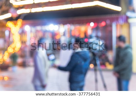 Blurred abstract of cameraman recording/videotaping a male journalist interviewing with local people at a pagoda in Ha Giang, Viet Nam. Colorful bokeh Lunar New Year decoration light is in background.