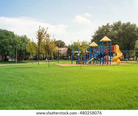 Colorful children playground activities in public park surrounded by green trees at sunset in Houston, Texas. Children run, slide, swing on modern playground. Urban neighborhood childhood concept.