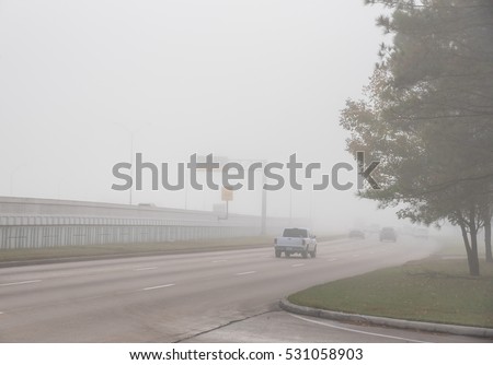 Morning foggy city road with traffic sign and car silhouette in Humble, Texas, US. Driving with caution in bad weather. Foggy hazy transportation hazard. Severe weather theme concept background.