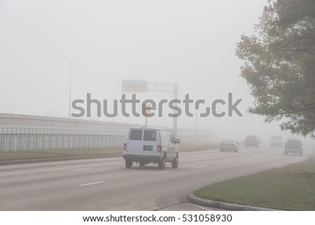 Morning foggy city road with traffic sign and car silhouette in Humble, Texas, US. Driving with caution in bad weather. Foggy hazy transportation hazard. Severe weather theme concept background.